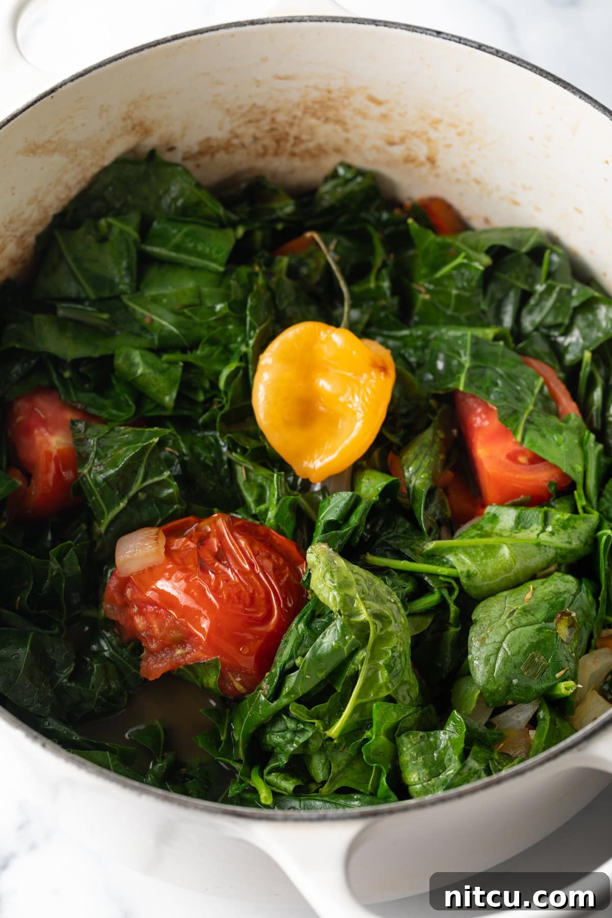 Pot loaded up with collard greens and tomato wedges. A large pot generously filled with fresh collard greens and vibrant tomato wedges, ready for simmering.