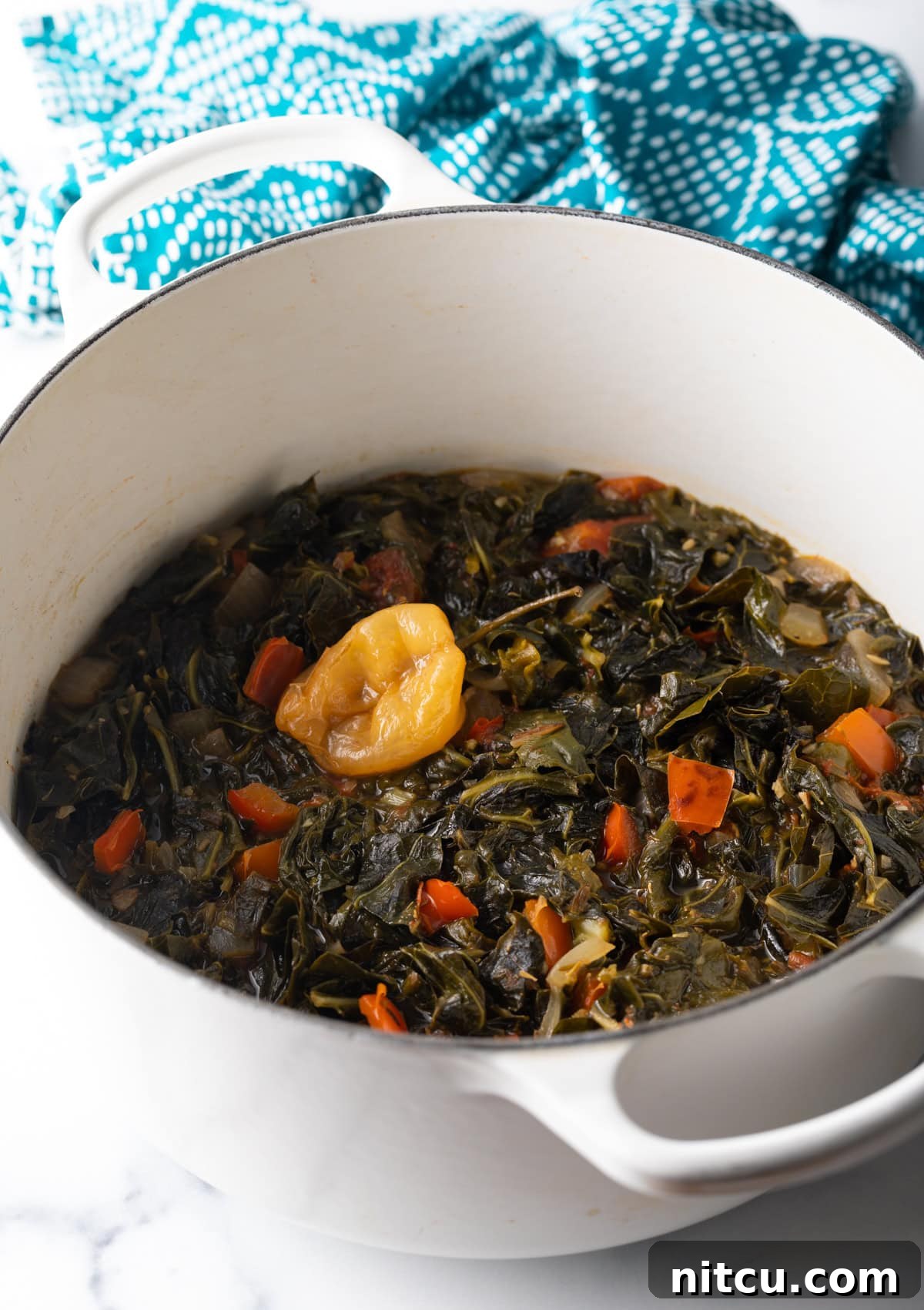 Top down view Jamaican stewed collard greens in a white pot. A top-down perspective of Jamaican stewed collard greens, showcasing the vibrant green and rich texture within a crisp white pot.