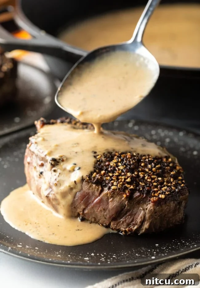 Spoon pouring cognac cream sauce over steak au poivre on a plate.
