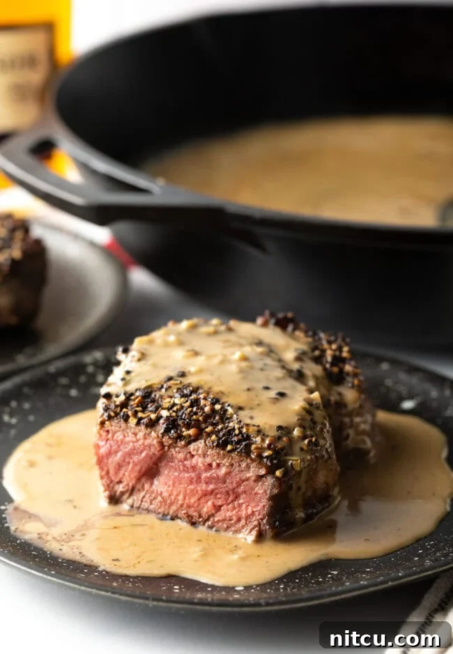 Steak on plate with cream sauce, bite taken to show medium rare cook on the inside.