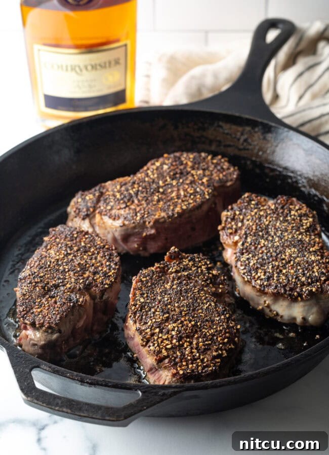 Steaks with pepper crust being seared in a cast iron skillet. 