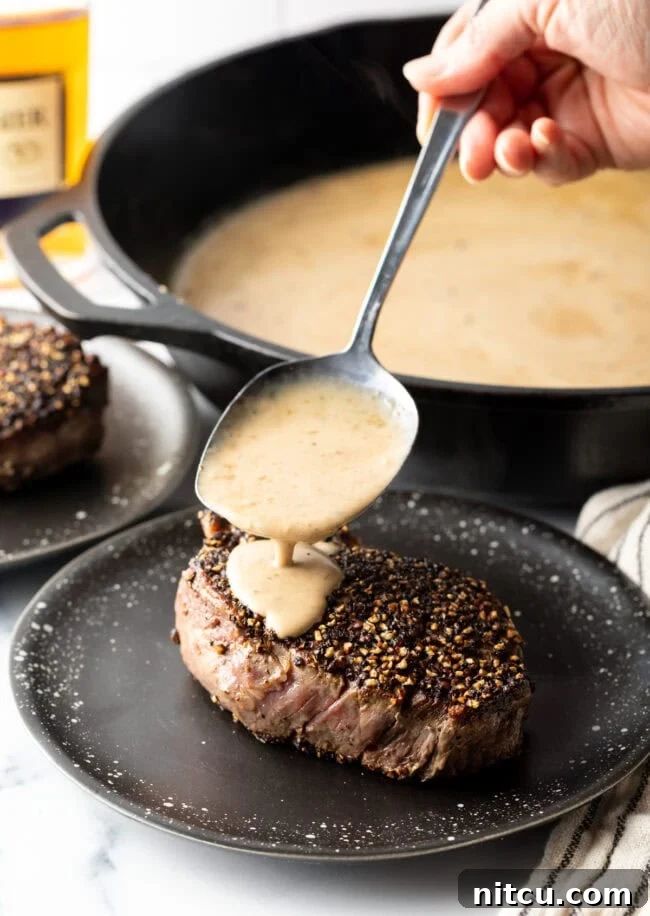 Hand spooning cognac steak sauce over the meat on a plate.