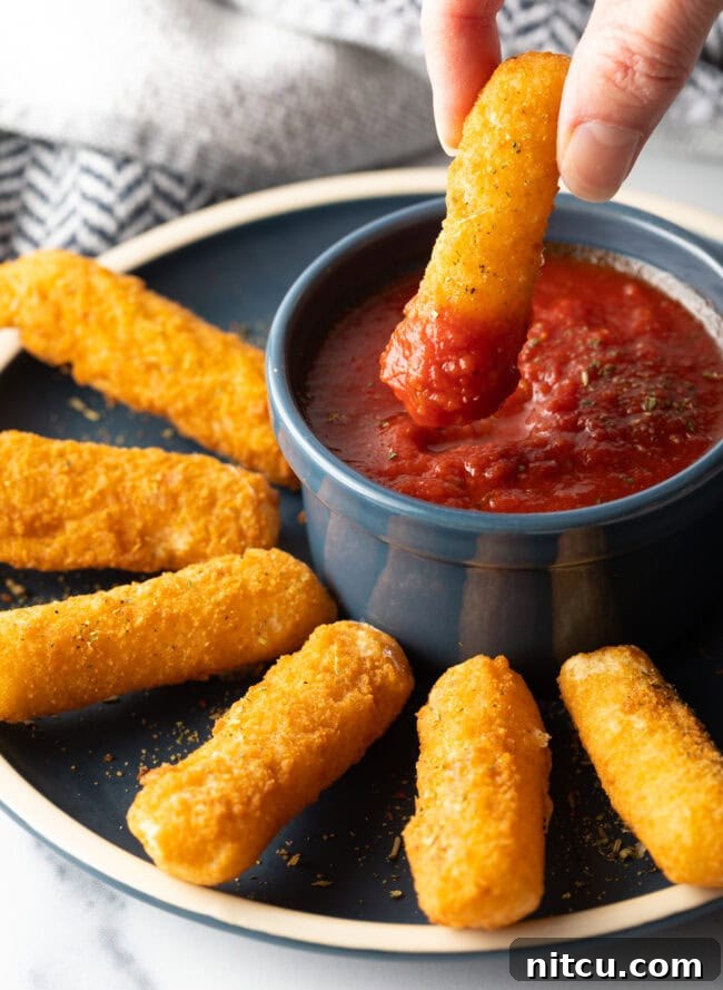 Homemade Air Fryer Mozzarella Sticks (or Frozen) - Hand dipping crispy air fried mozzarella cheese stick into marinara sauce.