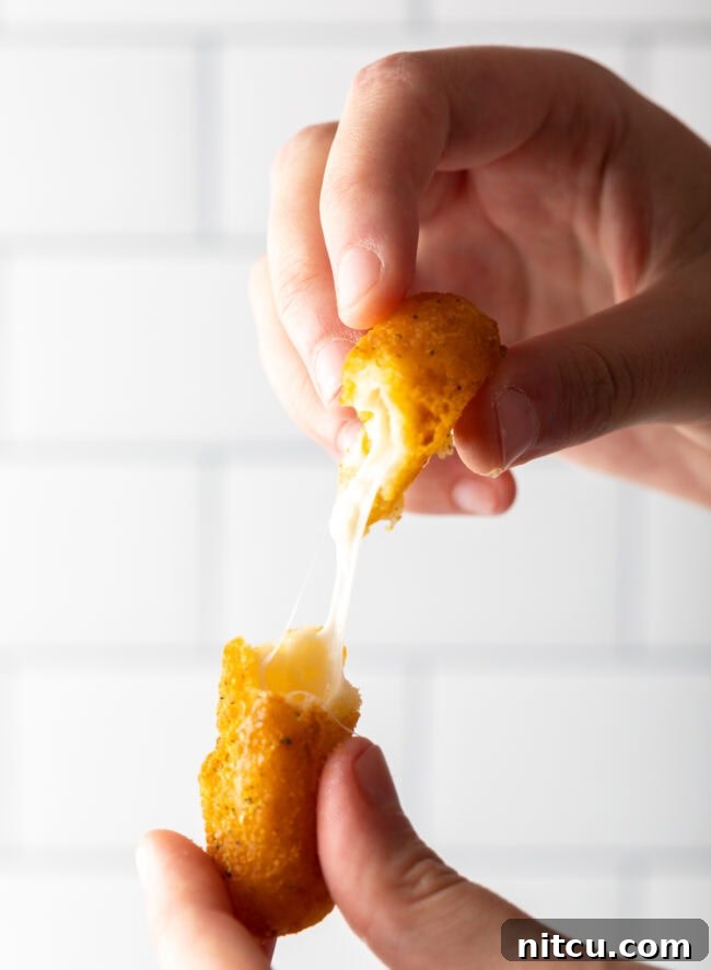 Hand pulling mozzarella cheese stick apart to show gooey cheese interior.