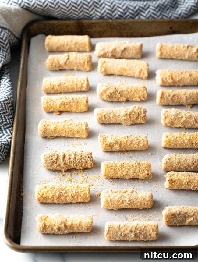 Breaded cheese sticks on a baking sheet lined with parchment paper.