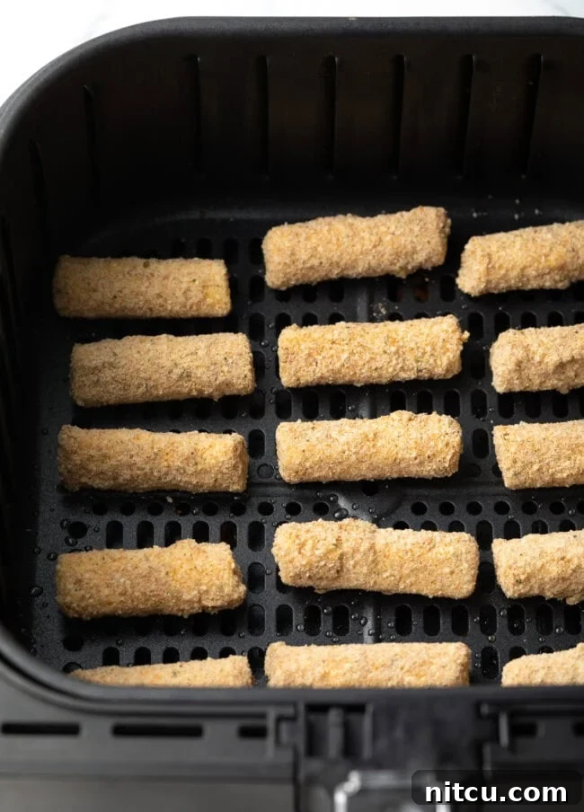 Breaded cheese sticks in an air fryer basket.