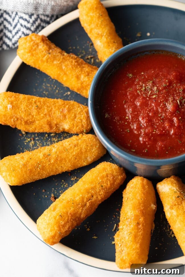 Top down crispy air fryer mozzarella cheese sticks fanned around ramekin of marinara sauce.