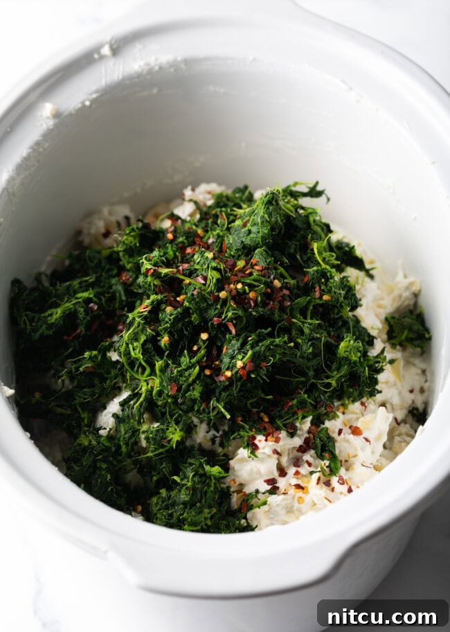 Cooked spinach and seasonings added to the slow cooker.