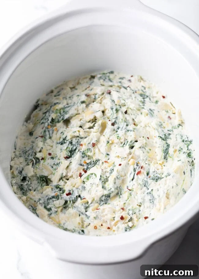 Spreading Crockpot Spinach Artichoke Dip mixture evenly in a slow cooker.