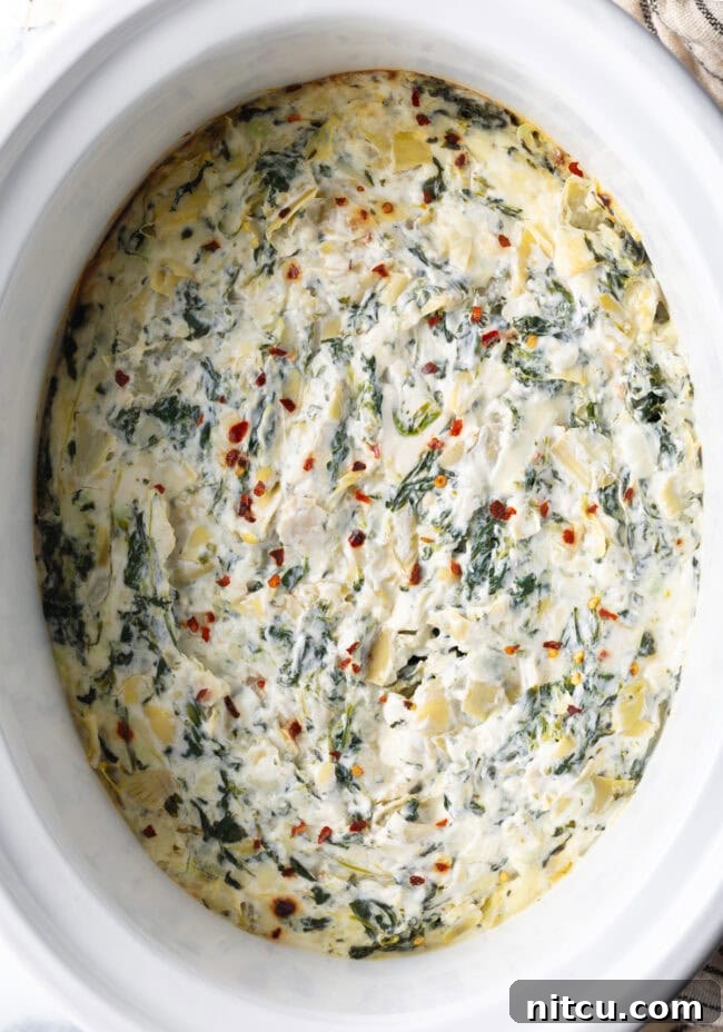 Top down view crock pot spinach artichoke dip in a slow cooker.