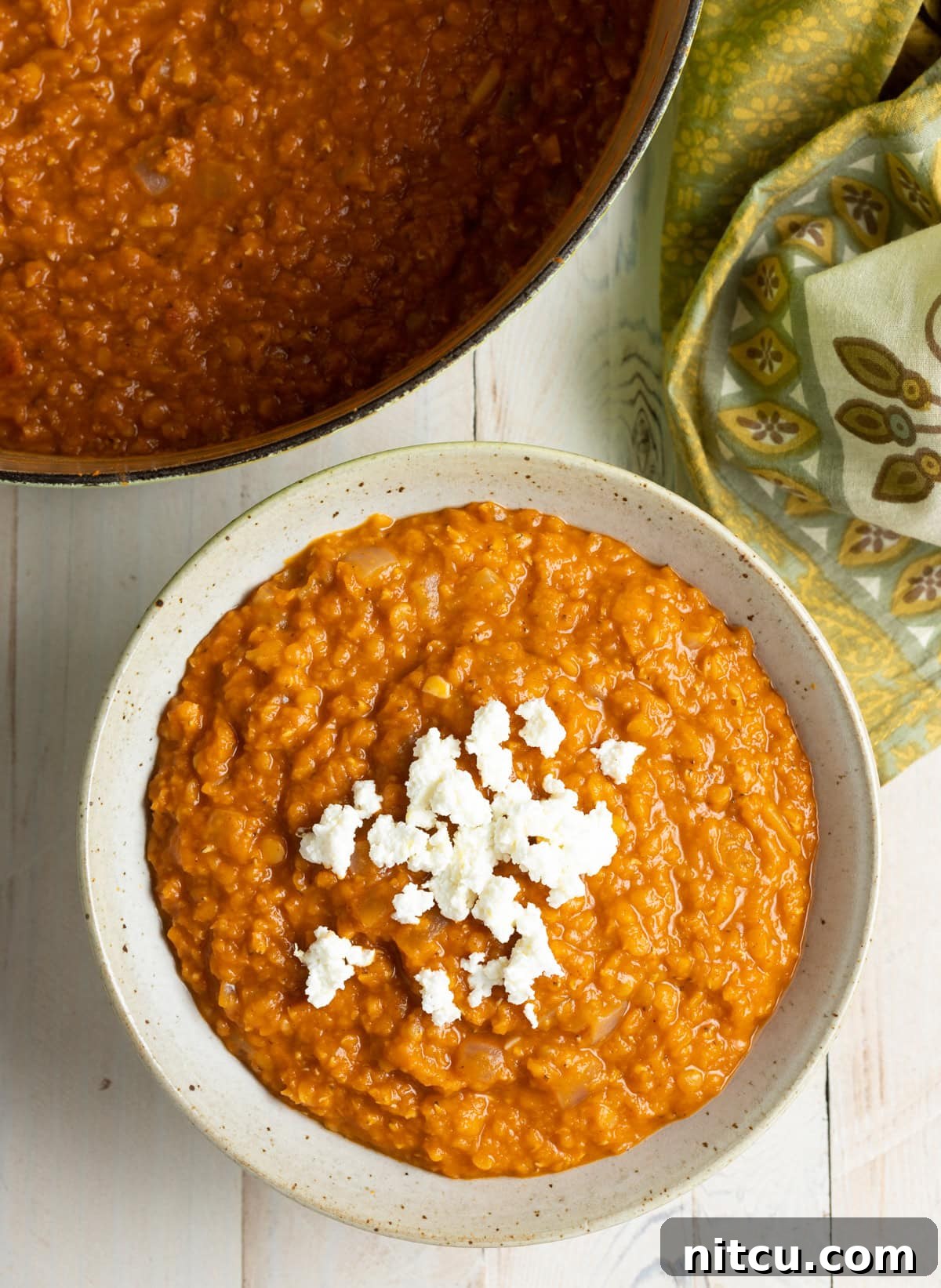 A top-down view of a steaming bowl of Ethiopian Red Lentil Stew (Misir Wot), richly spiced and topped with a creamy dollop of Ayib cheese.
