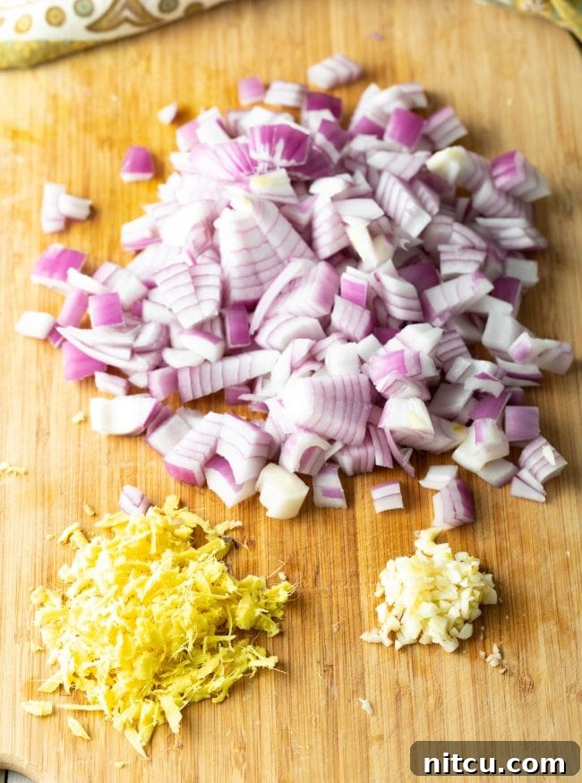 Ingredients for Misir Wot laid out on a cutting board, including red lentils, onions, garlic, ginger, and spices, awaiting preparation.
