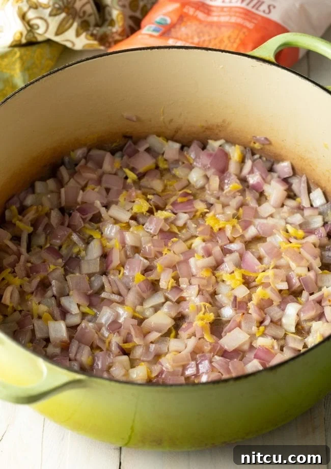 Close-up of onions, garlic, and ginger being sautéed in a pot, releasing their fragrant aromas as they soften.