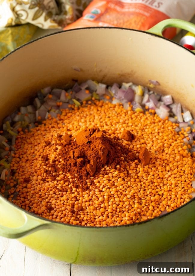 A pot filled with sautéed vegetables, covered with uncooked red lentils and a vibrant array of Ethiopian spices, ready for cooking.