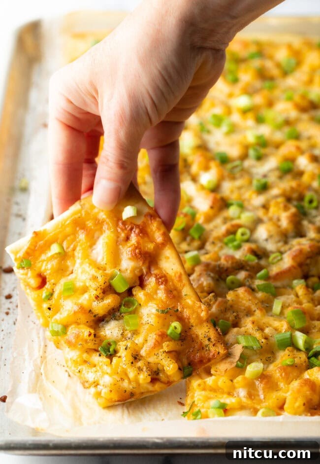 Hand lifting piece of mac and cheese pizza from full pizza.