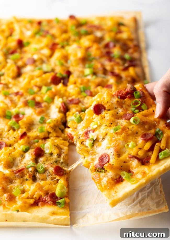 Hand removing a piece of mac and cheese pizza, cheese stretching.