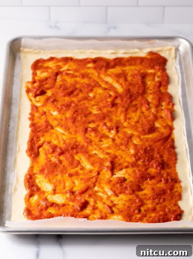 Dough rolled out in a rectangle with pizza sauce spread on top.
