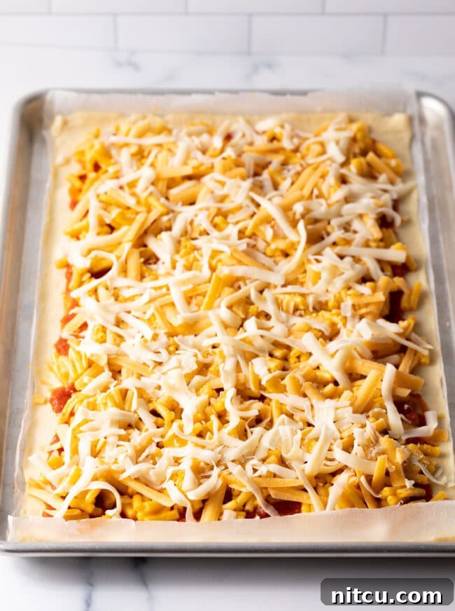 Shredded cheddar and mozzarella cheese sprinkled over mac and cheese layer.
