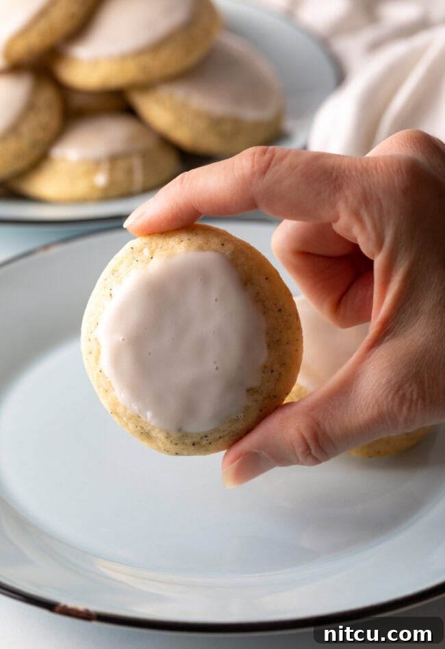A hand holding a perfectly dipped Earl Grey cookie towards the camera, showcasing its elegant glaze.