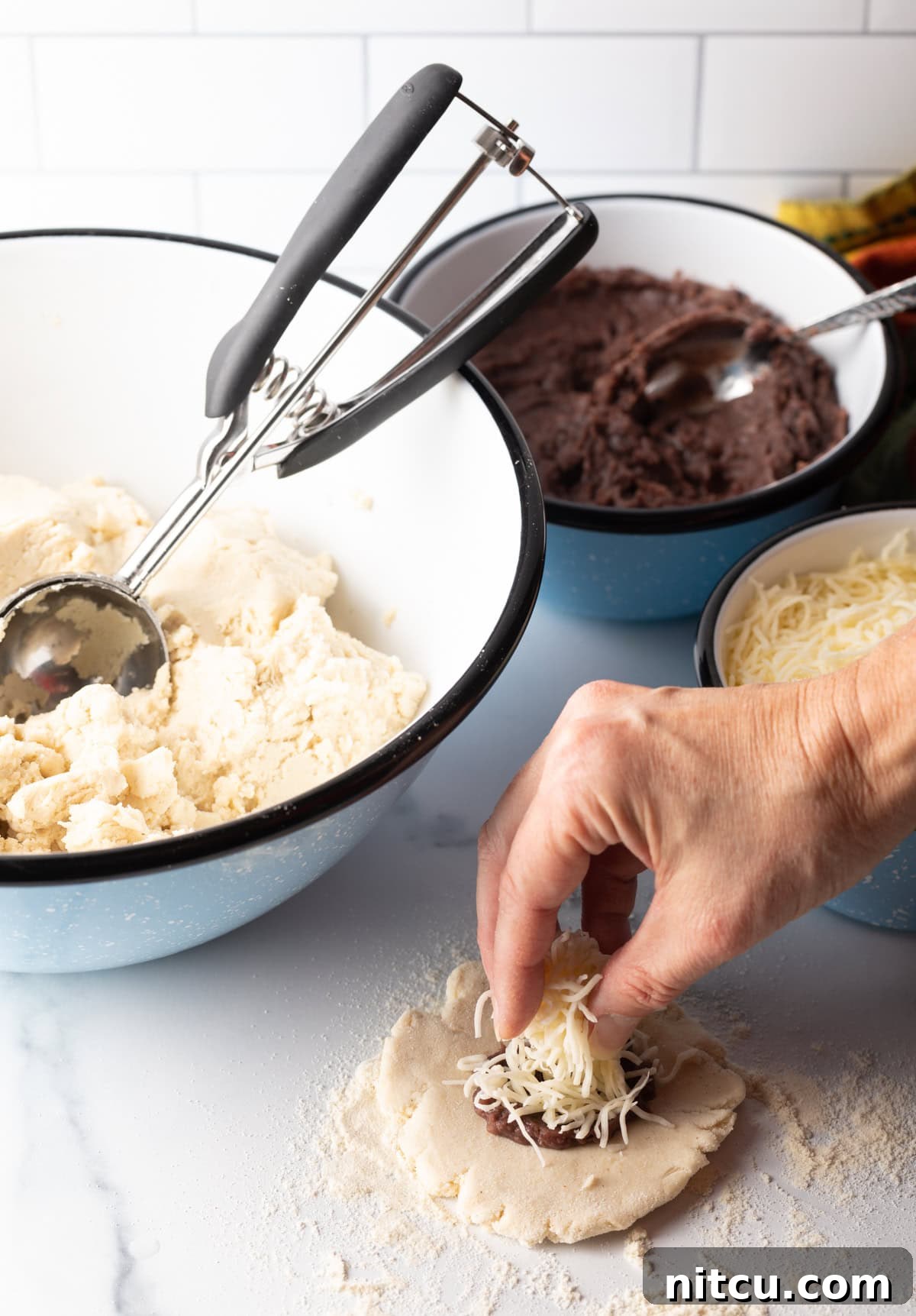 Hand adding shredded cheese on top of beans on flattened dough.