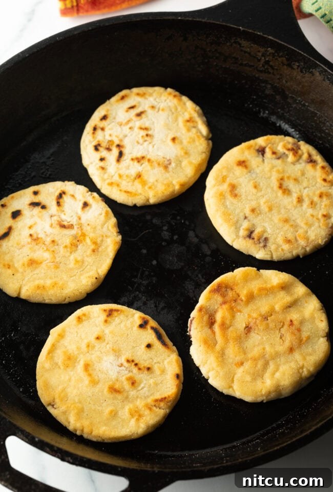 Pupusas cooking and sizzling in a cast iron skillet.
