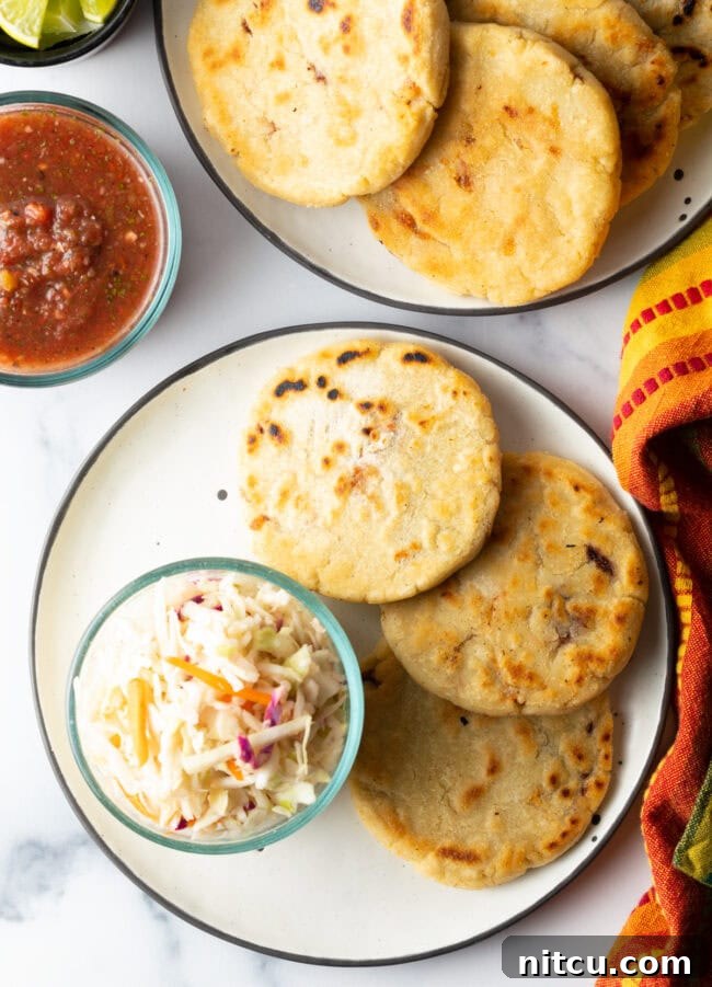 How to Make Pupusas - Top-down view of pupusas on a plate with cold slaw and various toppings.