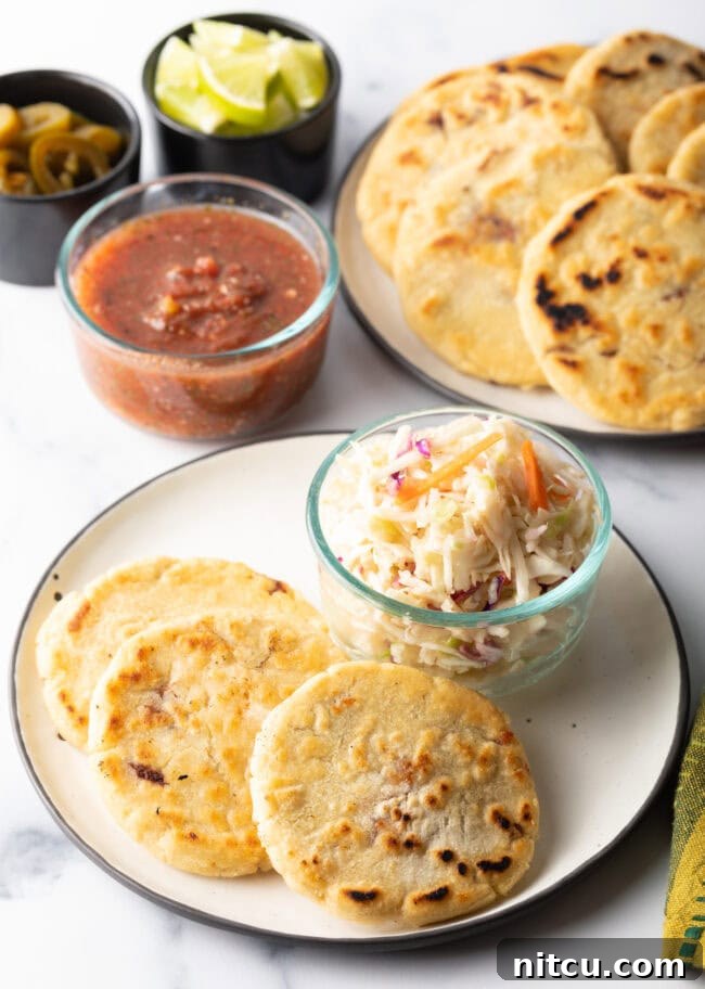 Three pupusas on a plate with a small glass dish of curtido slaw.