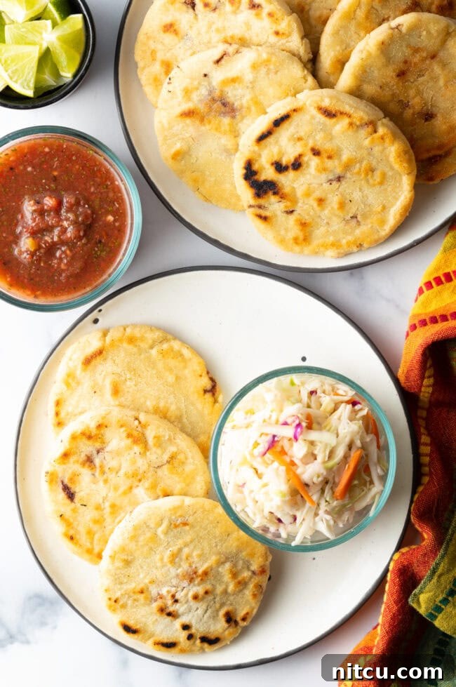 Top-down view of pupusas on a plate with fresh curtido slaw on the side.