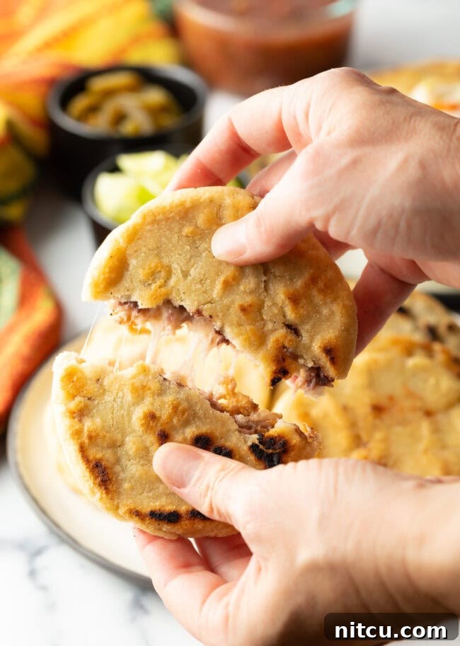 Hands tearing open a pupusa to reveal the melted cheese and beans inside.