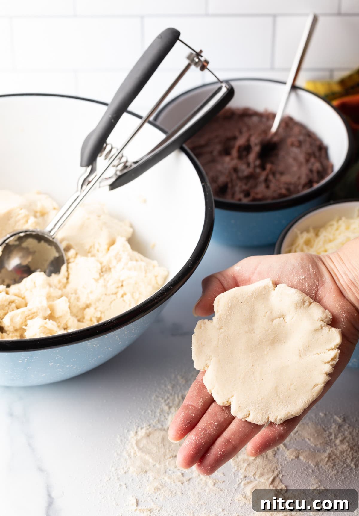 Hand holding a flattened disc of pupusa dough.