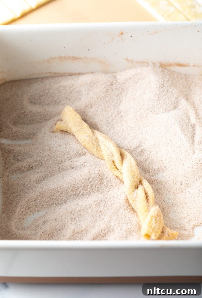 Braided puff pastry twists being coated in cinnamon sugar. 