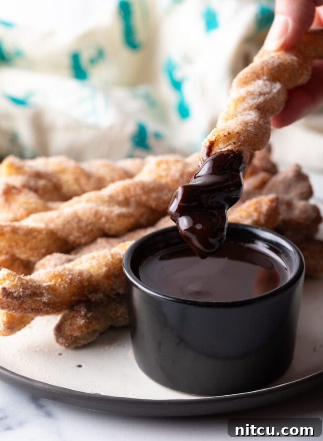 Hand dipping crunchy twist with sugar and cinnamon into a ramekin of chocolate sauce.