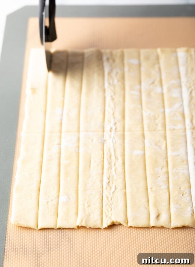 Puff pastry being sliced into slivers. 