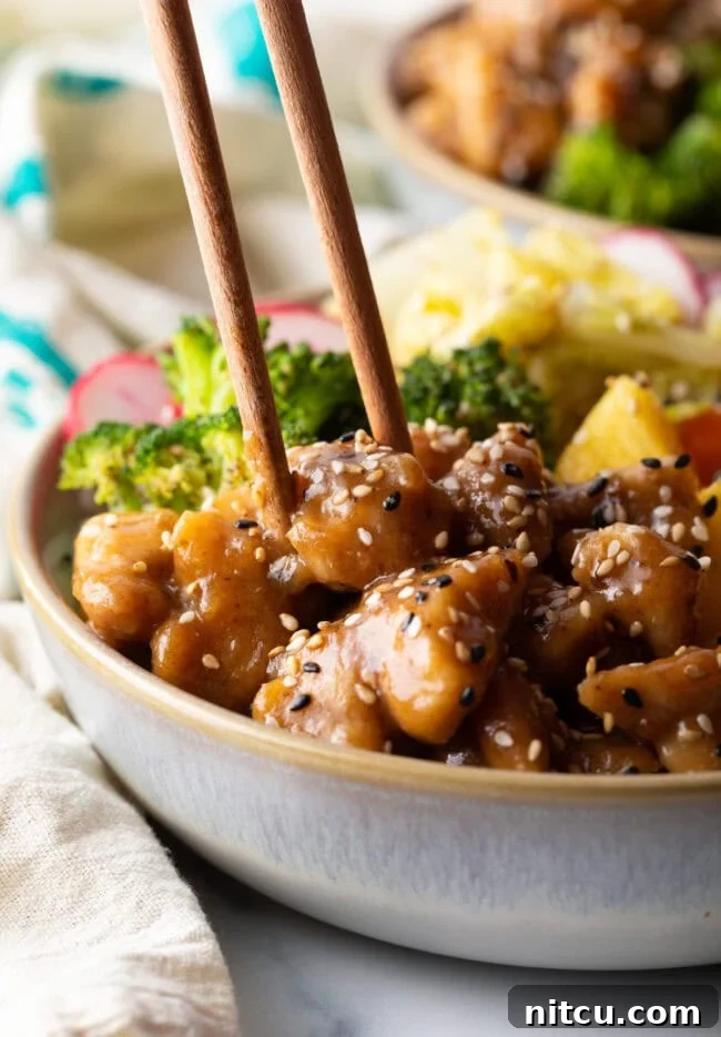 Chopsticks grabbing a piece of chicken from the bowl.