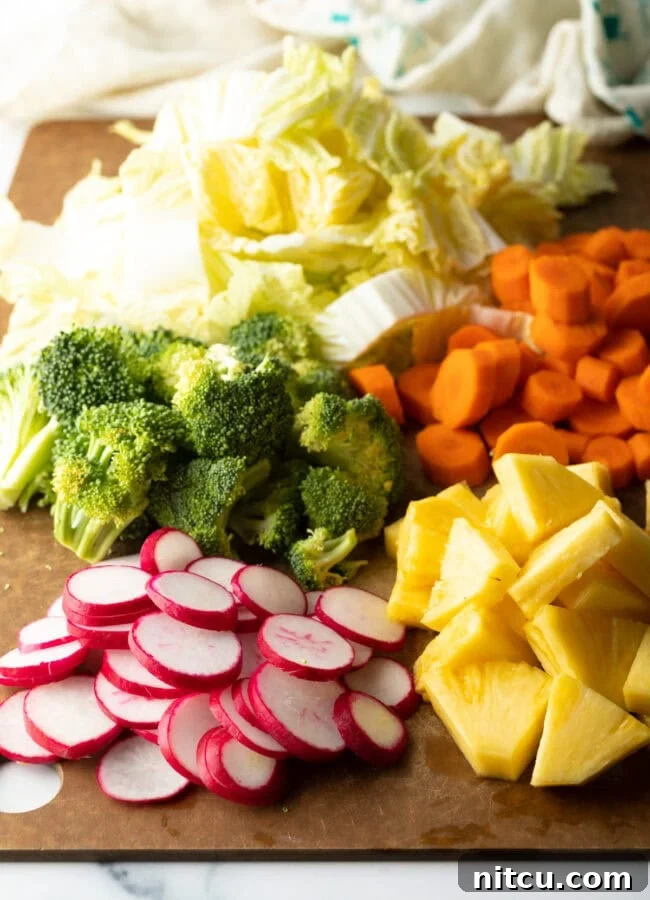 Fresh chopped veggies on a cutting board: broccoli, cabbage, carrots, pineapple, radishes.