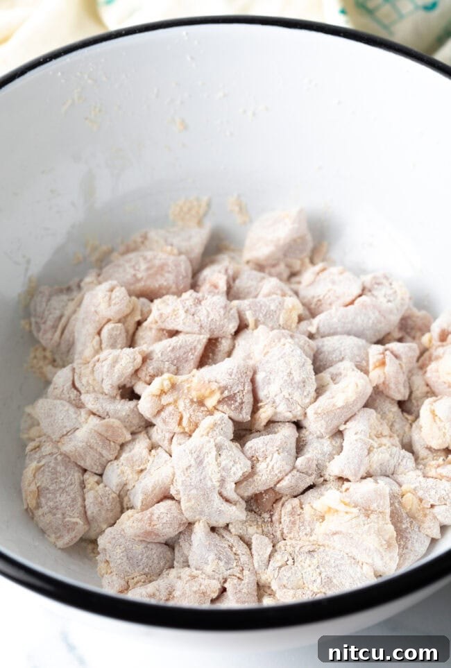 Pieces of chicken tossed with cornstarch in a bowl.