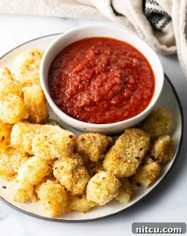 White plate with air fried cheese curds and white ramekin of marinara sauce.