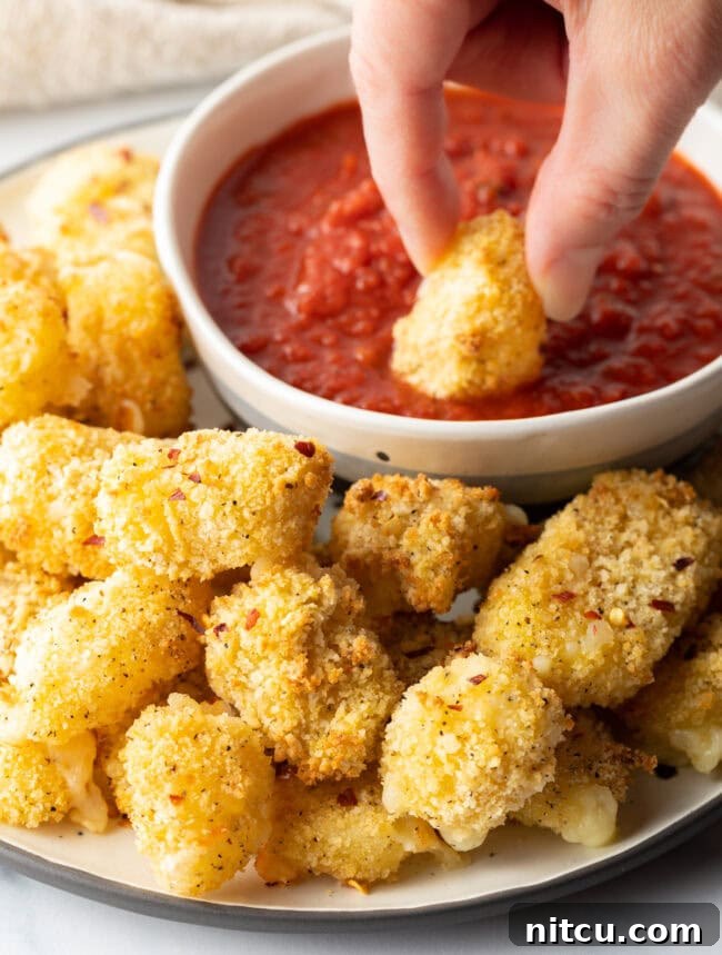 Hand dipping a curd into marinara sauce.