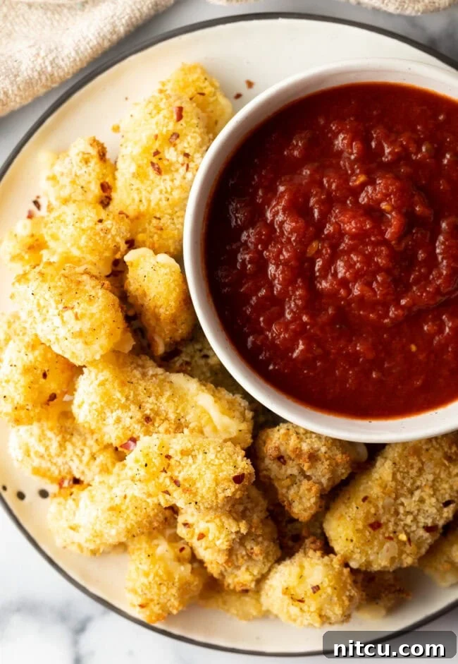Top down view air fryer cheese curds on a plate, with ramekin with marinara sauce.