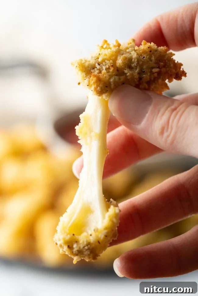 Hand pulling apart air fried cheese curds to show cheese inside.