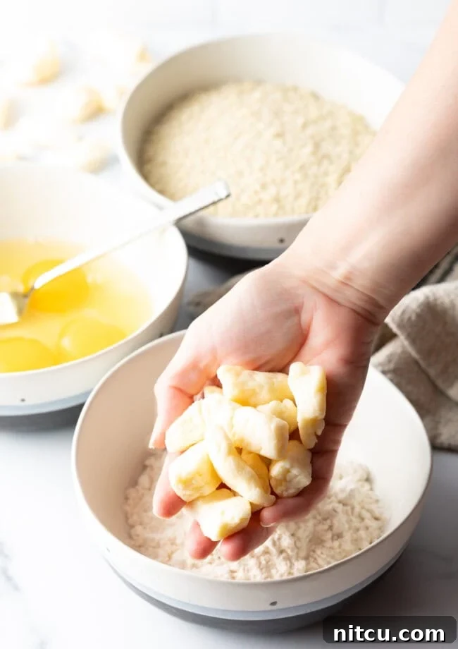 Hand holding pieces of white cheese curds above a bowl of flour.