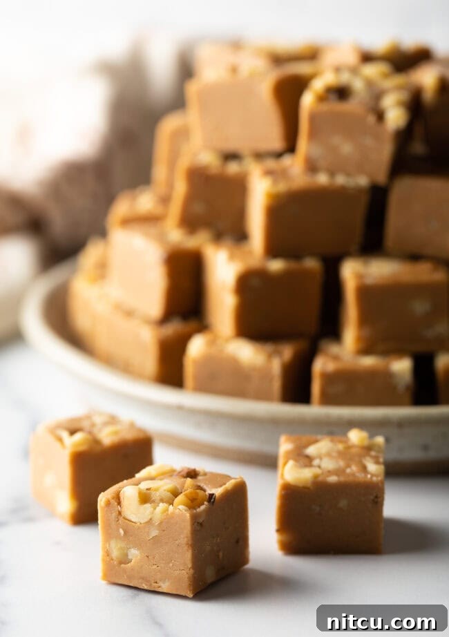 Squares of maple walnut fudge in front of a stack of fudge, highlighting the beautiful texture and rich color.