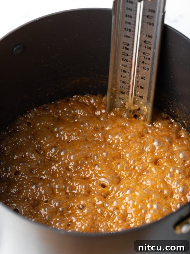 Maple syrup and cream mixture bubbling vigorously in a saucepot with a candy thermometer, indicating the soft ball stage.
