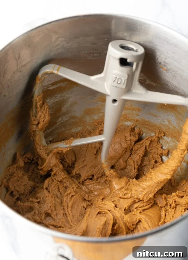 A standing mixer bowl with the paddle attachment, containing the maple fudge mixture that has begun to crystallize and lighten in color.