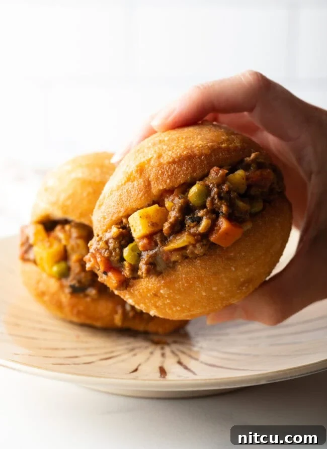 A hand holding a fat cake generously filled with savory minced meat, showcasing its fluffy interior.