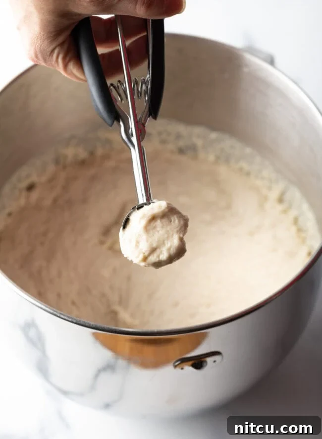 A hand using a 2-tablespoon scoop to portion out wet dough for frying.