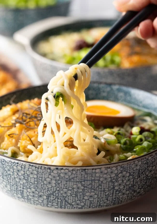 Hand with chopsticks, pulling noodles out of a soup bowl filled with katsu ramen.