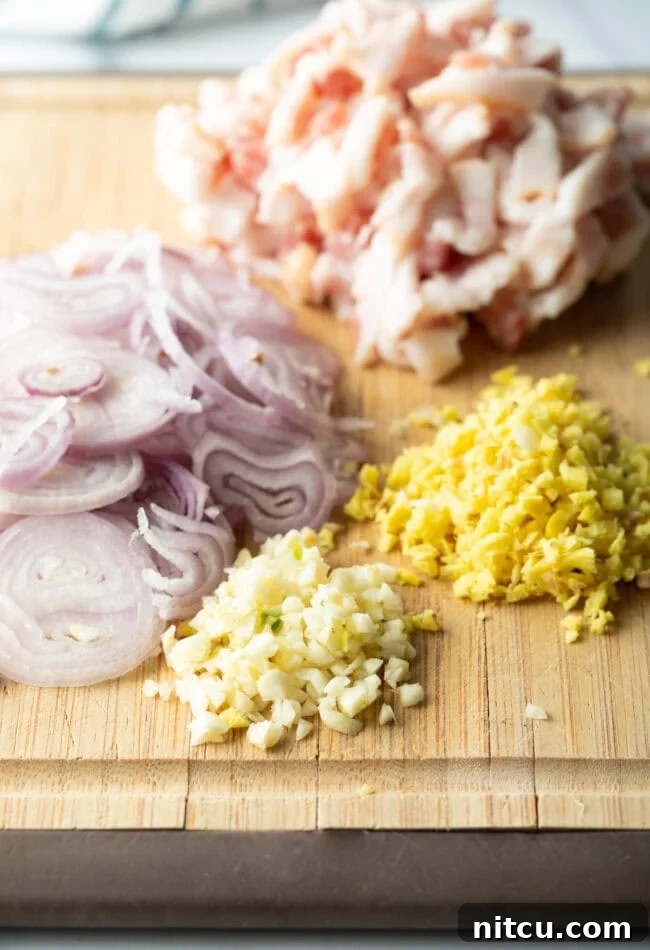 Minced garlic, ginger, sliced onion, and chicken pieces on a wood cutting board.
