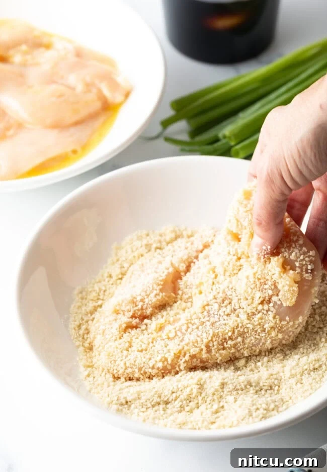 Hand dipping a chicken cutlet in the breadcrumbs.