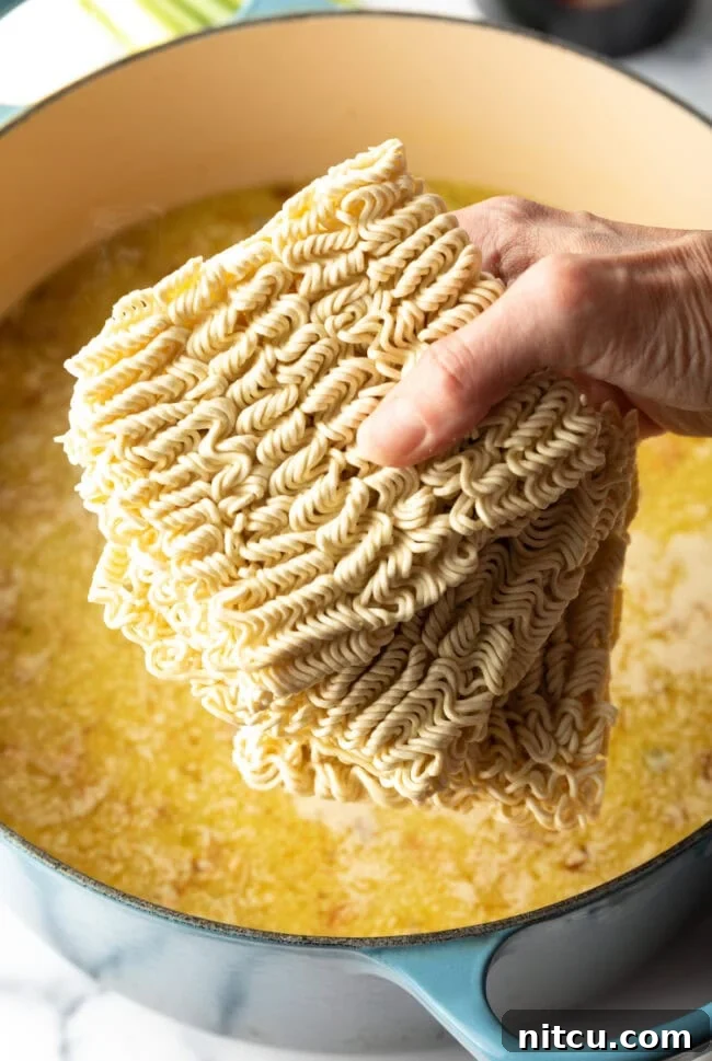 Hand holding blocks of ramen noodles above pot of boiling water.